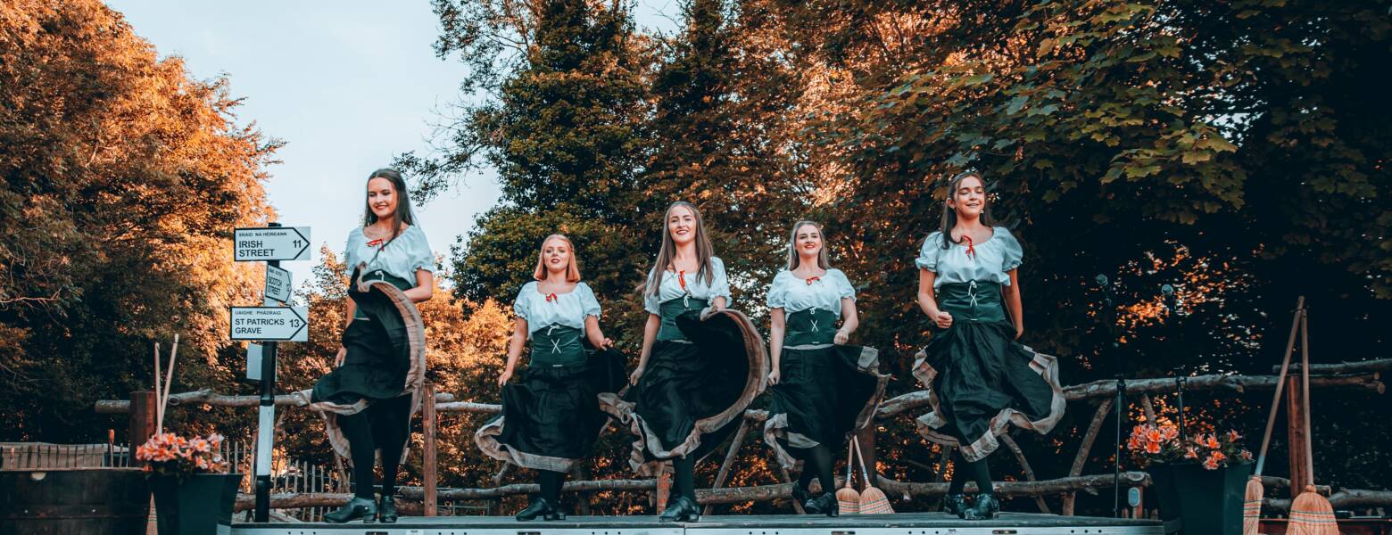five women performing Irish dancing on an outdoor stage for a tourism experience.